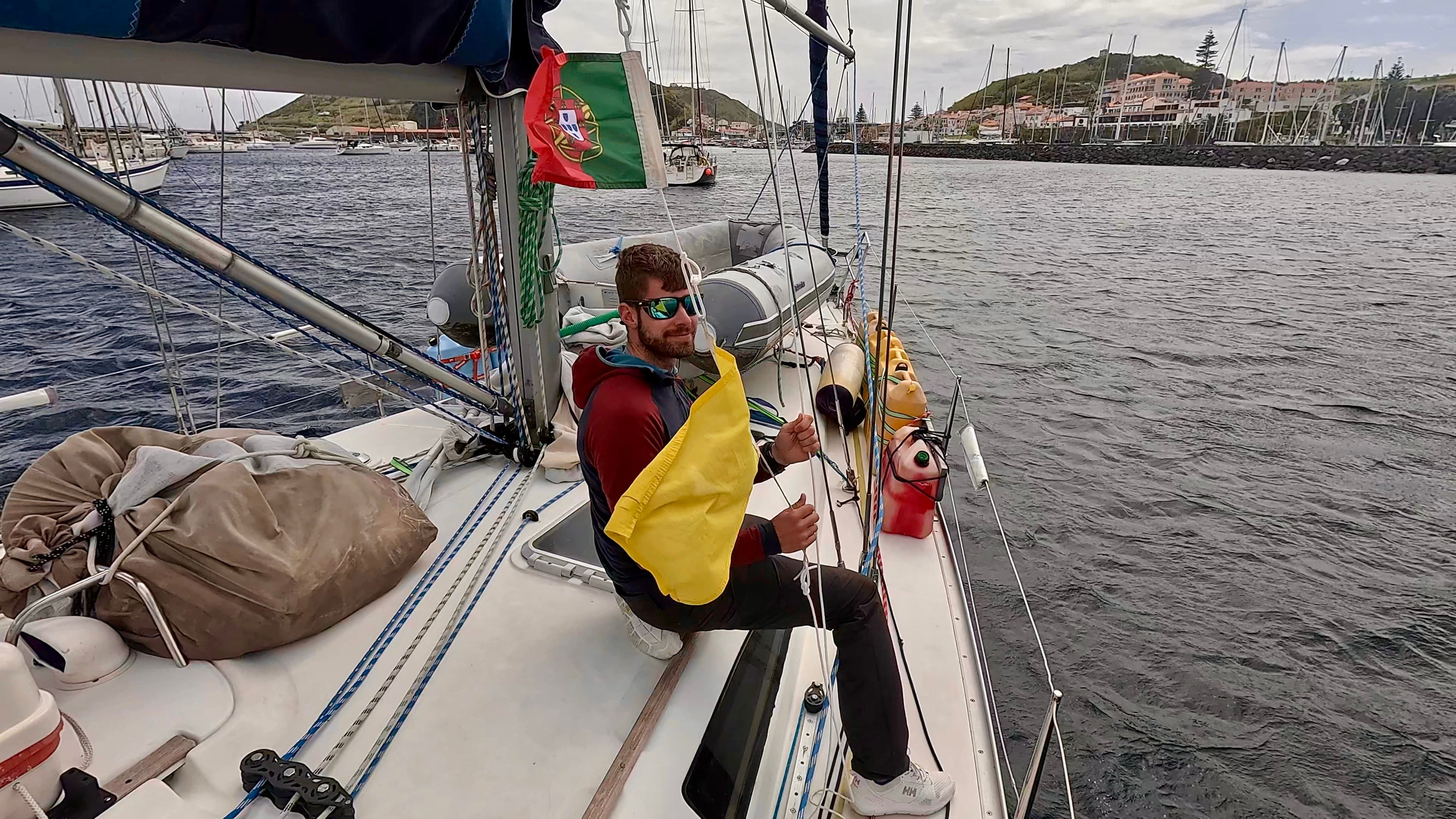Ein junger Mann setzt auf der Segelyacht Rocinante die Quarantäne- und die portugiesische Flagge nach der Überquerung des Atlantiks.