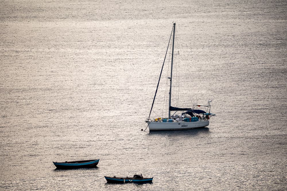 Die Segelyacht Rocinante in einer Ankerbucht vor einer karibischen Insel. Im Hintergrund ein sonnenbeschienener grüner Berg und darüber eine imposante Wolkenformation