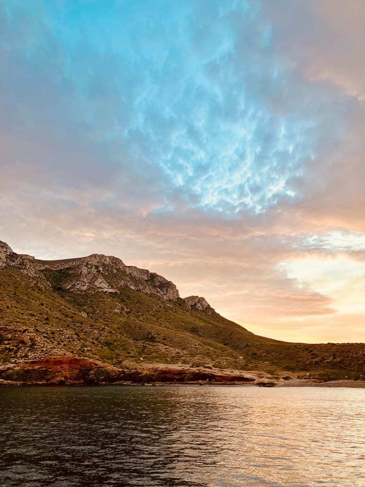 Sonnenuntergang an der spanischen Costa del Sol mit unnatürlich blau angestrahlten Wolken vor eine kargen Küste