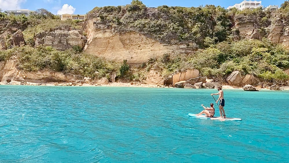 Zwei Menschen auf einem Stand-up-Paddleboard vor einem felsigen Ufer über türkisfarbenem Wasser
